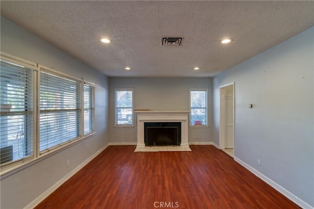unfurnished living room with visible vents, plenty of natural light, wood finished floors, and a textured ceiling