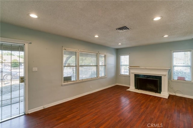 unfurnished living room featuring a fireplace, wood finished floors, visible vents, and a healthy amount of sunlight