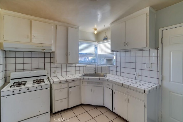 kitchen featuring white range with gas cooktop, white cabinetry, tile counters, and sink