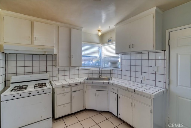 kitchen with white gas stove, tile counters, a sink, and under cabinet range hood