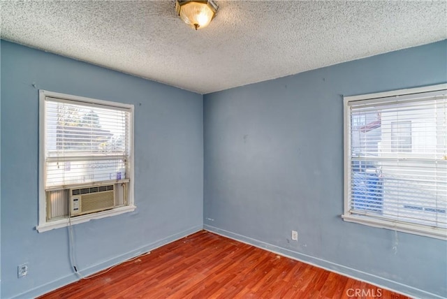 empty room with cooling unit, baseboards, a textured ceiling, and wood finished floors