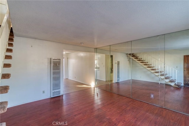 spare room featuring a textured ceiling, visible vents, baseboards, wood finished floors, and stairs