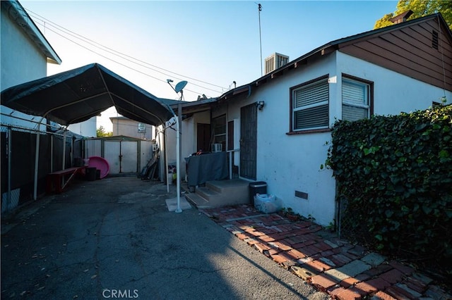 view of home's exterior featuring a detached carport, stucco siding, crawl space, a storage unit, and an outbuilding