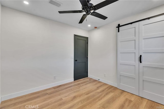 unfurnished bedroom with a closet, a barn door, ceiling fan, and light hardwood / wood-style flooring