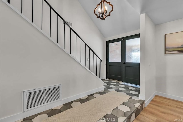 foyer entrance with a notable chandelier, vaulted ceiling, light wood-type flooring, and french doors