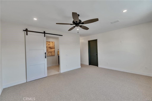 empty room featuring a barn door, light carpet, and ceiling fan