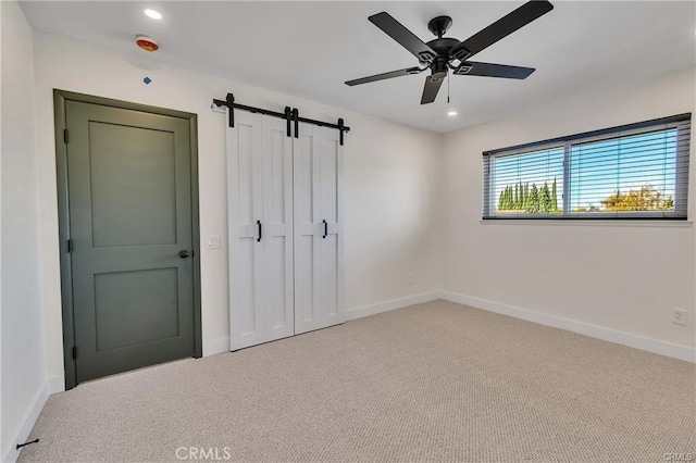 unfurnished bedroom with carpet flooring, a barn door, ceiling fan, and a closet