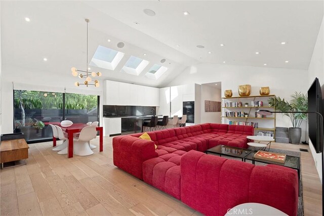 living room featuring a notable chandelier, light hardwood / wood-style floors, high vaulted ceiling, and a skylight