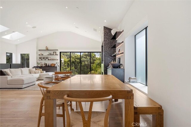 dining space with light wood-type flooring, a skylight, and high vaulted ceiling