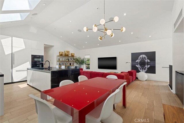 dining area with a skylight, sink, light hardwood / wood-style floors, and an inviting chandelier