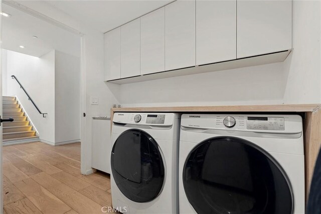 laundry area with cabinets, independent washer and dryer, and light wood-type flooring