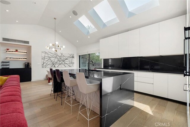 kitchen with a skylight, a center island with sink, light hardwood / wood-style flooring, white cabinetry, and a breakfast bar area