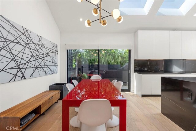 dining space with vaulted ceiling with skylight, a chandelier, and light hardwood / wood-style flooring