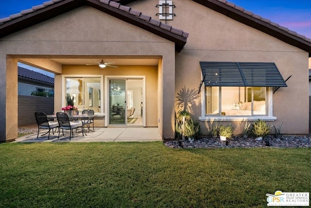 back house at dusk with a lawn, ceiling fan, and a patio