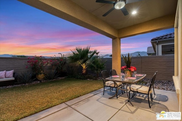 patio terrace at dusk featuring a lawn and ceiling fan