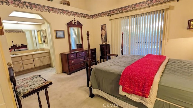 bedroom featuring ensuite bathroom, light colored carpet, arched walkways, and a sink
