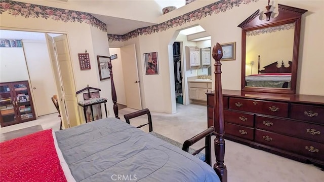 bedroom with a sink, arched walkways, ensuite bath, and light carpet