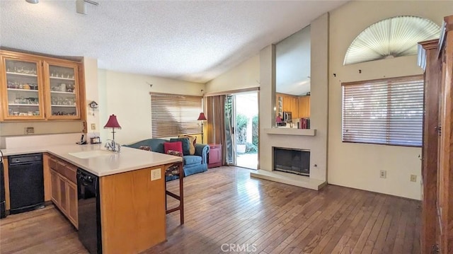 kitchen featuring vaulted ceiling, dishwasher, a large fireplace, sink, and kitchen peninsula