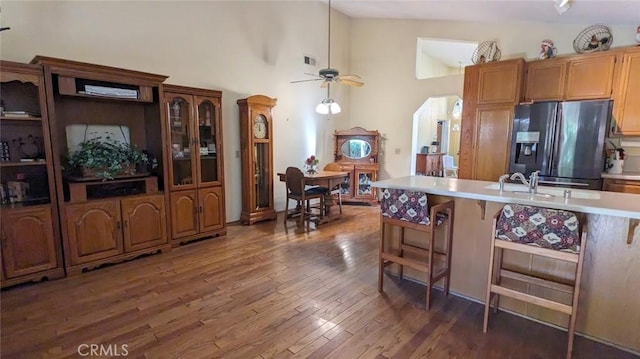 kitchen with ceiling fan, high vaulted ceiling, dark hardwood / wood-style floors, stainless steel fridge, and a breakfast bar