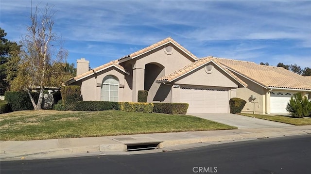 mediterranean / spanish-style house featuring a tile roof, stucco siding, an attached garage, and a chimney