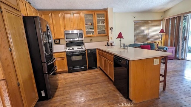 kitchen featuring sink, kitchen peninsula, a textured ceiling, a breakfast bar, and black appliances