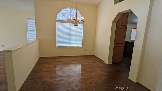 unfurnished dining area with dark wood-type flooring, arched walkways, baseboards, and a chandelier