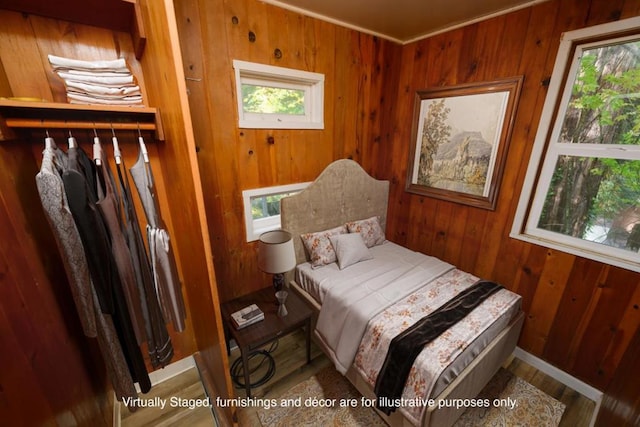 bedroom with multiple windows, wooden walls, and wood-type flooring