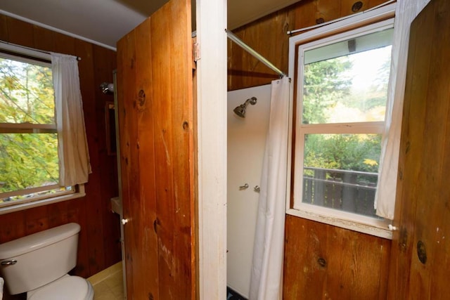 bathroom with wooden walls, a shower with shower curtain, and toilet