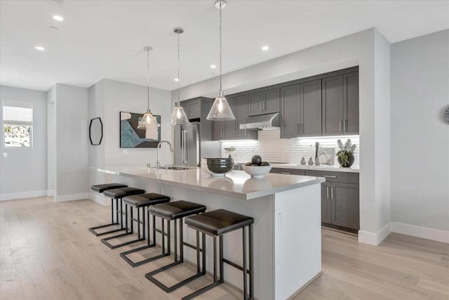 kitchen featuring a kitchen bar, light wood-type flooring, backsplash, sink, and gray cabinets