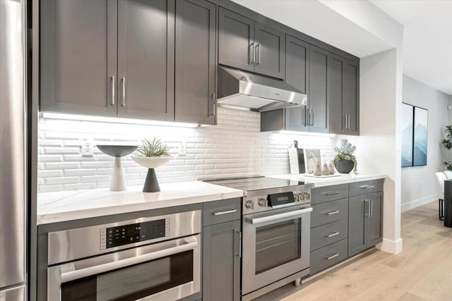 kitchen featuring backsplash, light stone counters, light hardwood / wood-style floors, stainless steel appliances, and gray cabinets