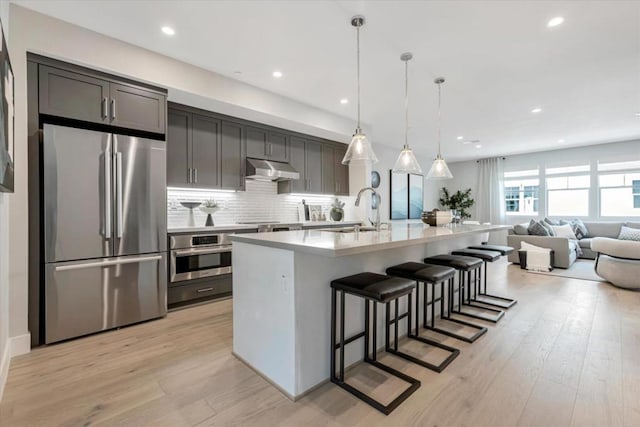 kitchen featuring a kitchen breakfast bar, light wood-type flooring, stainless steel appliances, sink, and an island with sink