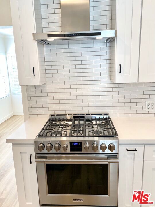 kitchen with white cabinetry, wall chimney exhaust hood, decorative backsplash, high end stainless steel range, and light wood-type flooring