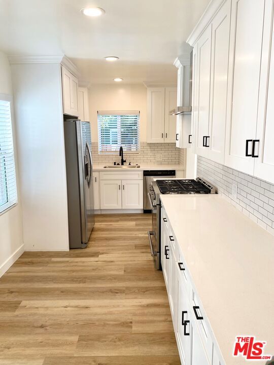 kitchen with backsplash, white cabinets, sink, light hardwood / wood-style flooring, and appliances with stainless steel finishes