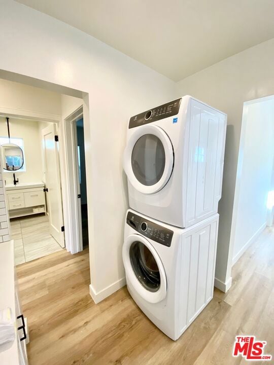 clothes washing area with stacked washing maching and dryer and light hardwood / wood-style floors