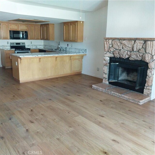 kitchen featuring sink, light wood-type flooring, stainless steel electric range oven, kitchen peninsula, and a breakfast bar area