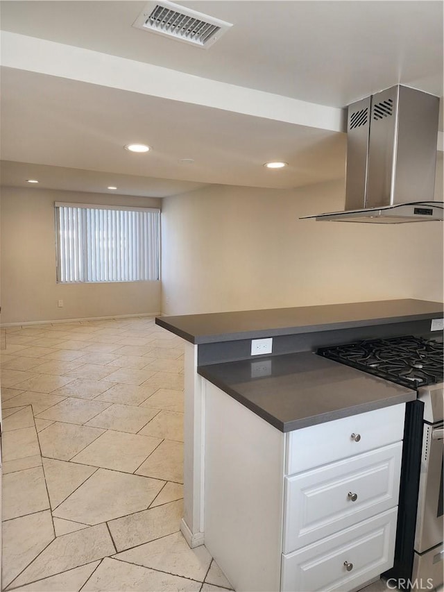 kitchen featuring dark countertops, visible vents, wall chimney range hood, white cabinets, and stainless steel gas range