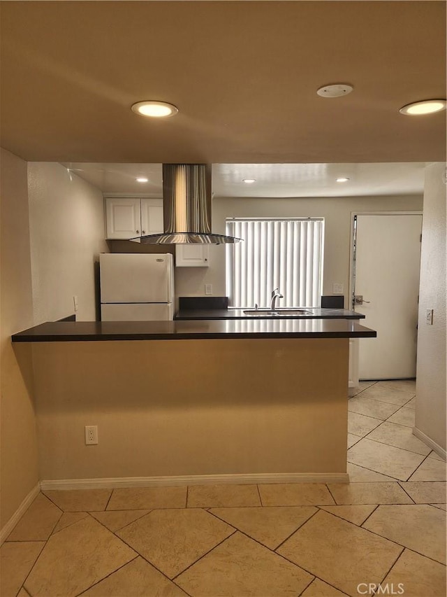 kitchen with light tile patterned flooring, kitchen peninsula, white fridge, island exhaust hood, and white cabinets