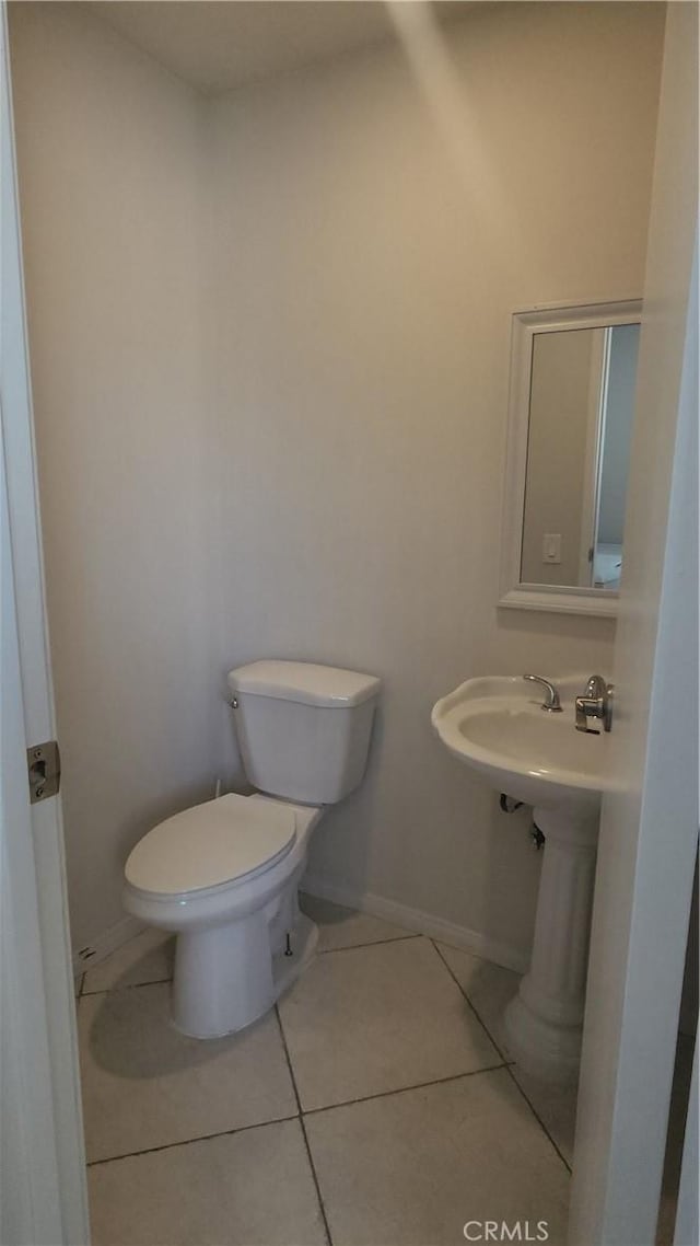 half bath featuring tile patterned floors, toilet, and baseboards