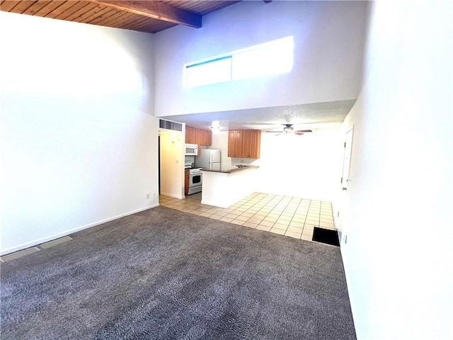 unfurnished living room featuring beam ceiling, ceiling fan, a towering ceiling, light tile patterned floors, and wood ceiling