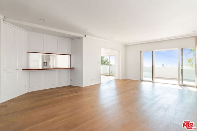 unfurnished living room featuring a healthy amount of sunlight, ornamental molding, and light hardwood / wood-style floors