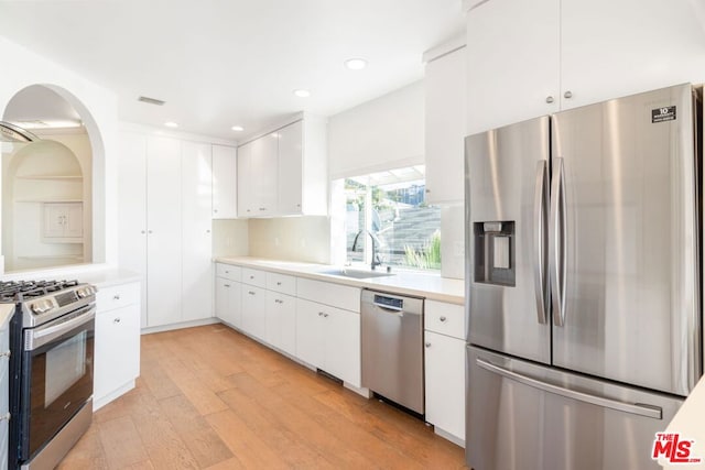 kitchen with sink, stainless steel appliances, white cabinetry, and light hardwood / wood-style flooring