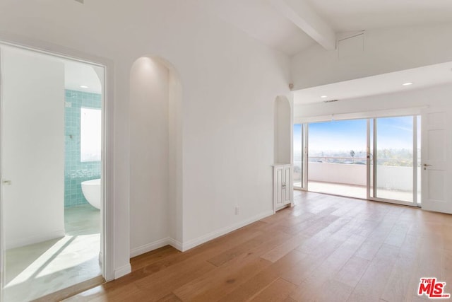 unfurnished room featuring light wood-type flooring and lofted ceiling with beams