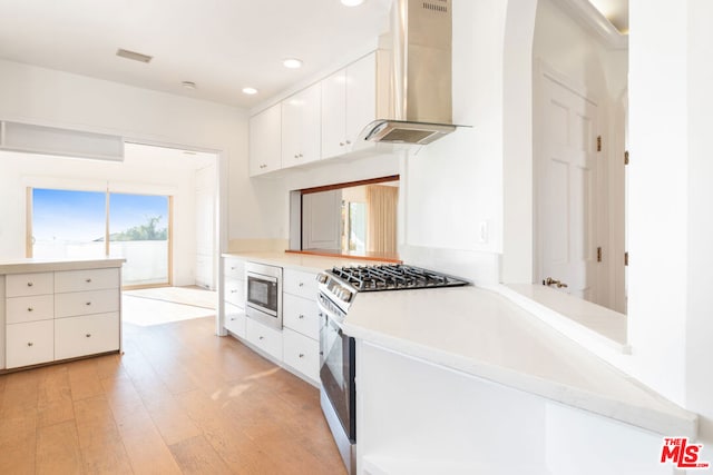 kitchen featuring kitchen peninsula, appliances with stainless steel finishes, wall chimney exhaust hood, white cabinets, and light hardwood / wood-style floors