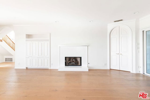 unfurnished living room with a fireplace, crown molding, and light wood-type flooring