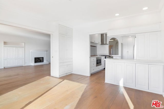 kitchen featuring white cabinets, wall chimney exhaust hood, built in appliances, and light wood-type flooring