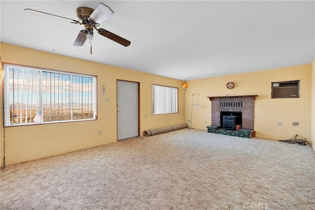 unfurnished living room with carpet flooring, a wood stove, and ceiling fan