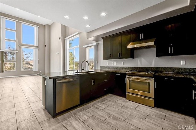 kitchen with appliances with stainless steel finishes, dark stone countertops, kitchen peninsula, and sink