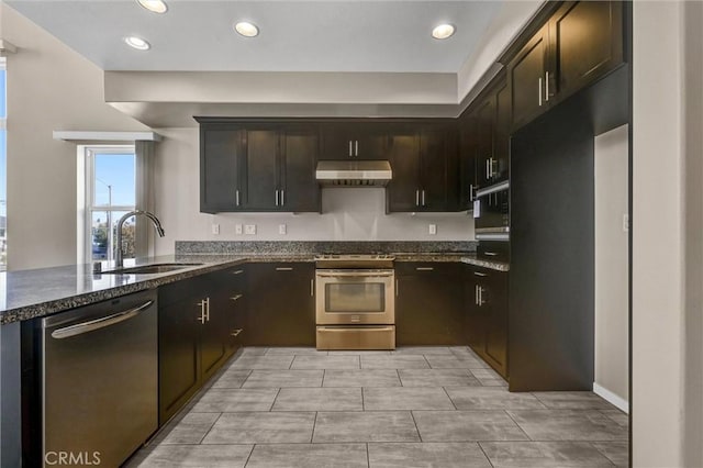 kitchen with kitchen peninsula, dark brown cabinets, sink, stainless steel appliances, and dark stone counters