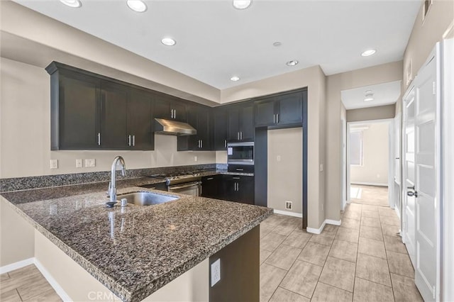 kitchen with appliances with stainless steel finishes, dark stone countertops, kitchen peninsula, and sink