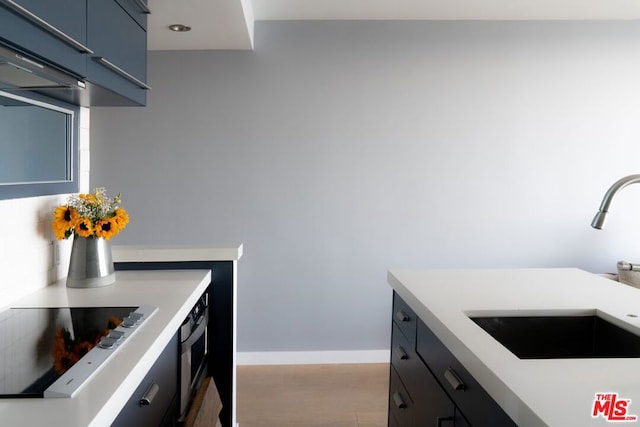 kitchen featuring stainless steel oven, sink, blue cabinets, stovetop, and light hardwood / wood-style floors